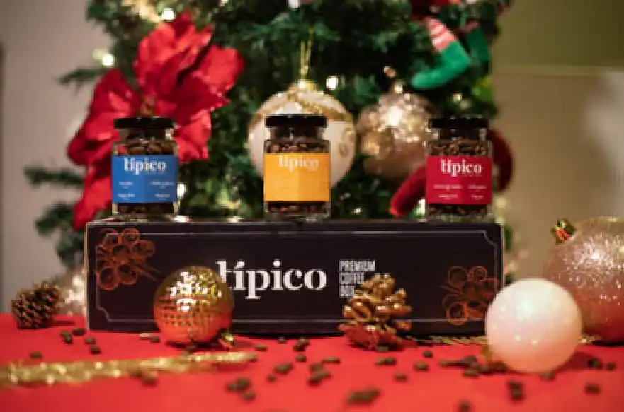 Caja de regalo de café Típico con tres frascos de café, rodeada de decoración navideña.