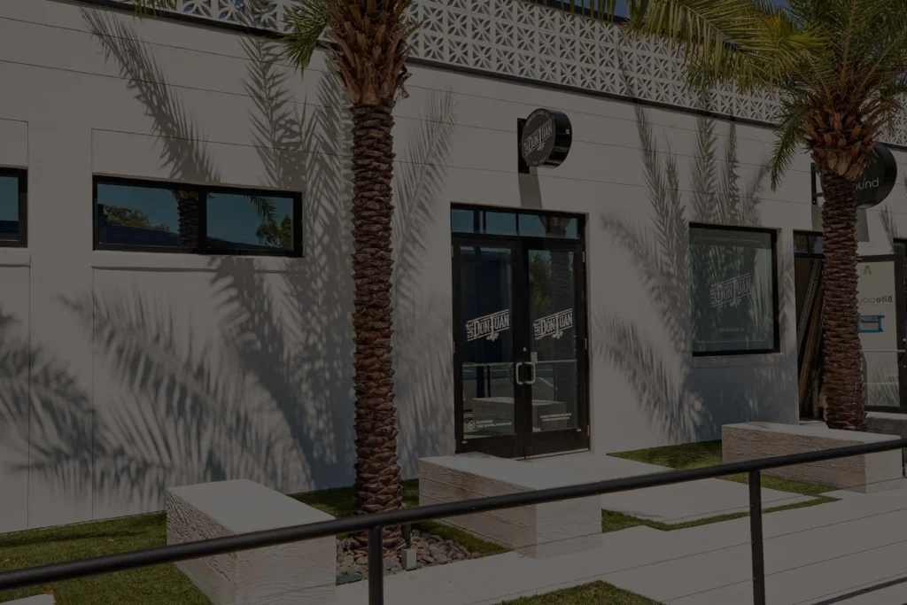 Entrada principal de la tienda Café Don Juan en Winter Park con letrero y dos palmas, mostrada con un filtro oscuro semitransparente.