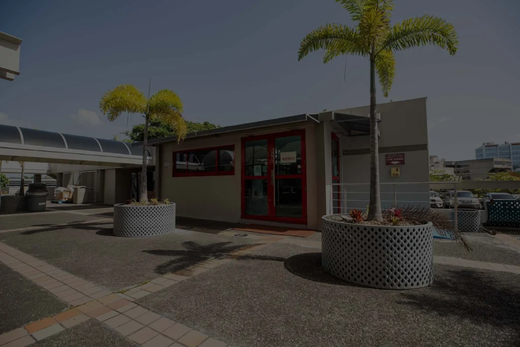 Entrada principal de la tienda Café Don Juan en Ciencias Médicas con filtro oscuro semitransparente, mostrando puertas de vidrio y dos palmas.