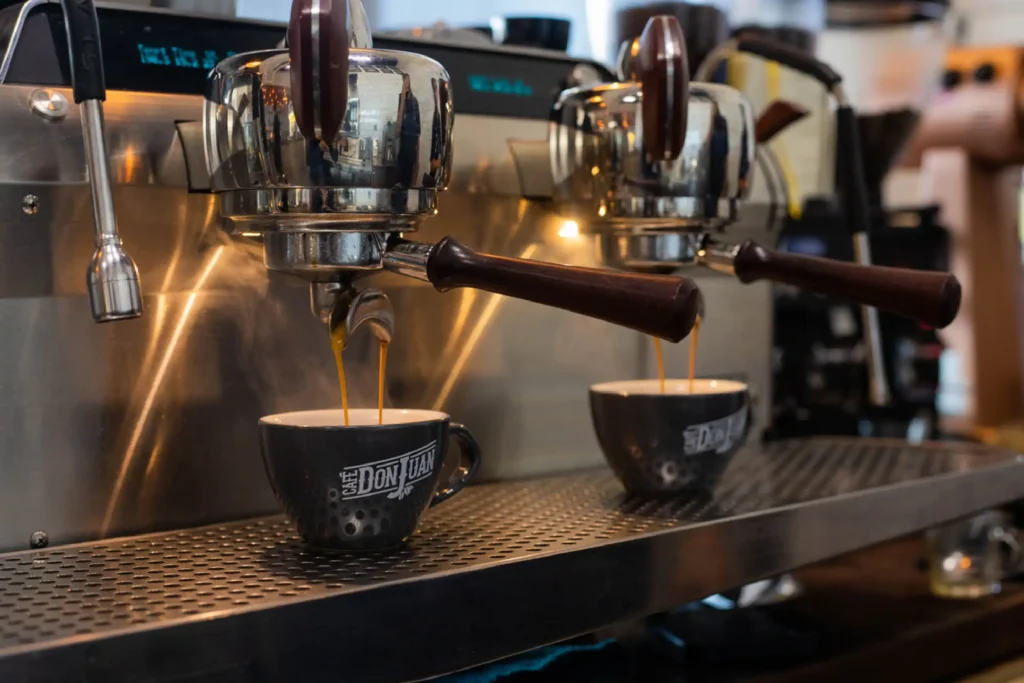 Dos tazas negras con el logo de Café Don Juan recibiendo espresso de una máquina profesional.