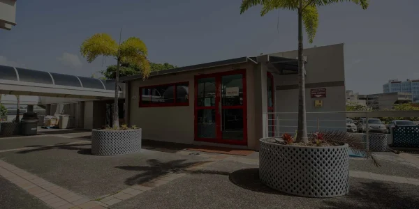 Entrada principal de la tienda Café Don Juan en Ciencias Médicas con filtro oscuro semitransparente, mostrando puertas de vidrio y dos palmas.