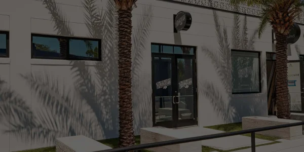 Entrada principal de la tienda Café Don Juan en Winter Park con letrero y dos palmas, mostrada con un filtro oscuro semitransparente.