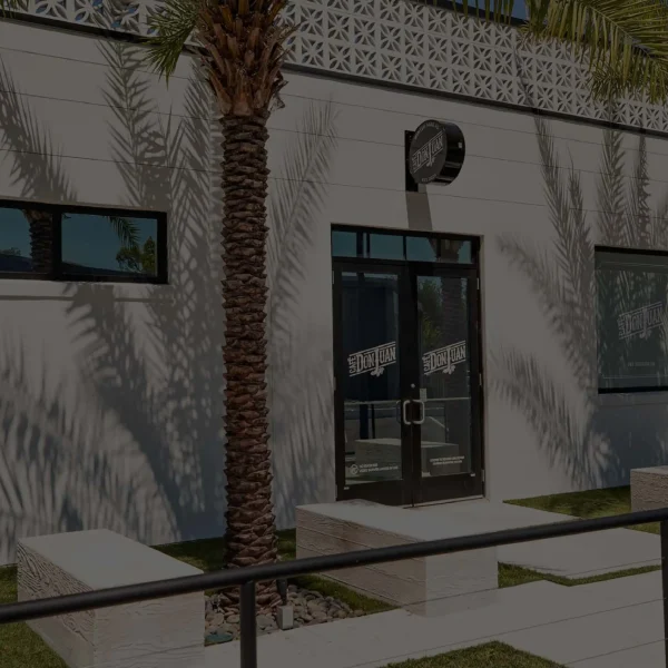 Entrada principal de la tienda Café Don Juan en Winter Park con letrero y dos palmas, mostrada con un filtro oscuro semitransparente.