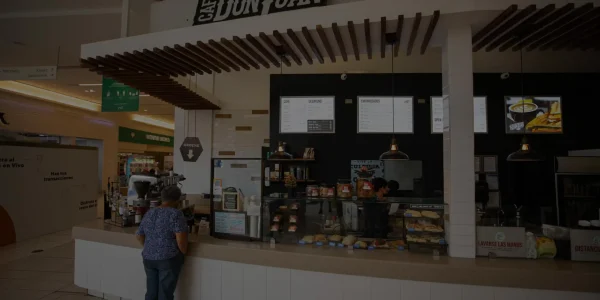 Tienda de Café Don Juan dentro del centro comercial Plaza Rio Hondo con clientes de pie frente al mostrador y vitrinas de productos, mostrada con un filtro oscuro semitransparente.